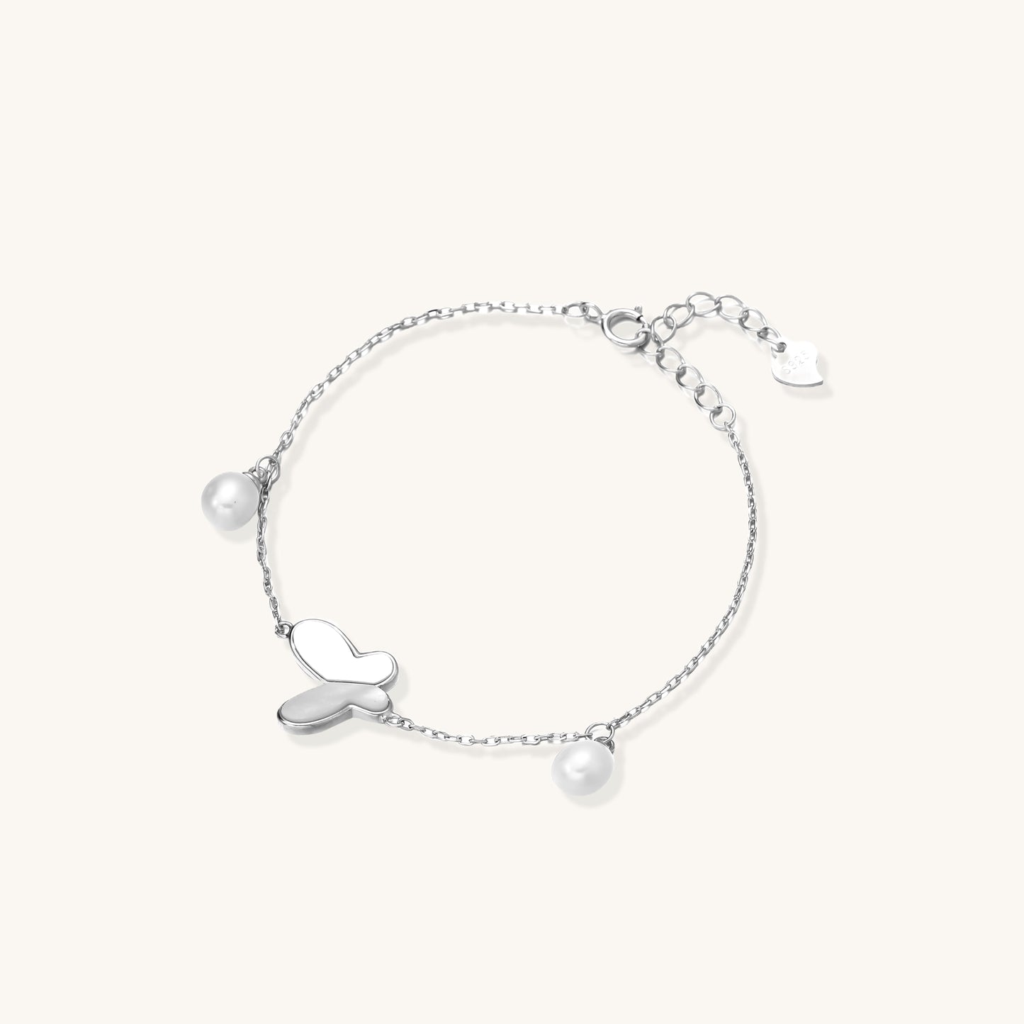 Dainty sterling silver chain bracelet with heart charm and freshwater pearl dangles on white background.