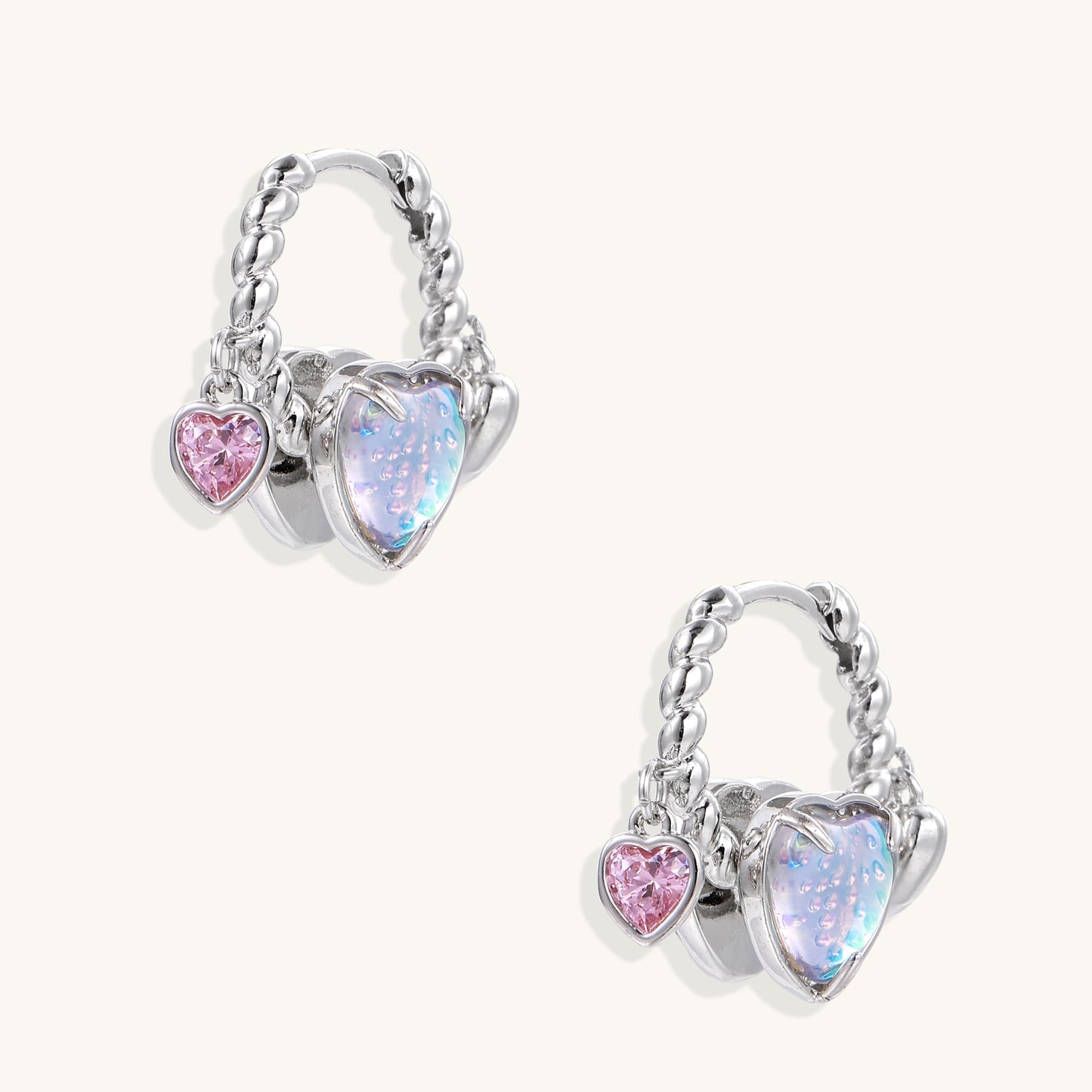 Gold-plated brass hoop earrings with three heart charms including iridescent turquoise and pink hearts on white background.