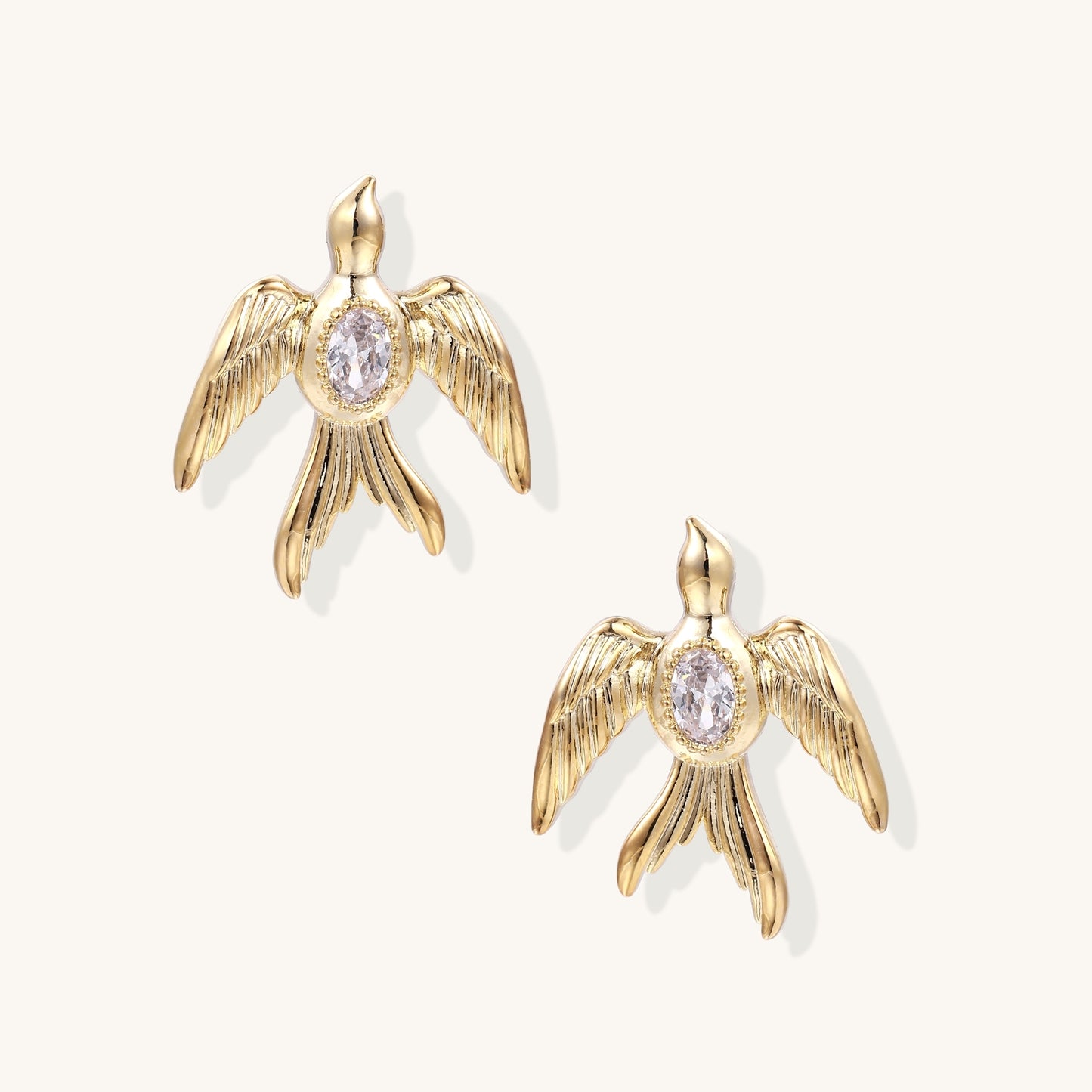 Pair of gold-plated eagle stud earrings with spread wings and purple zirconia center stones on white background.