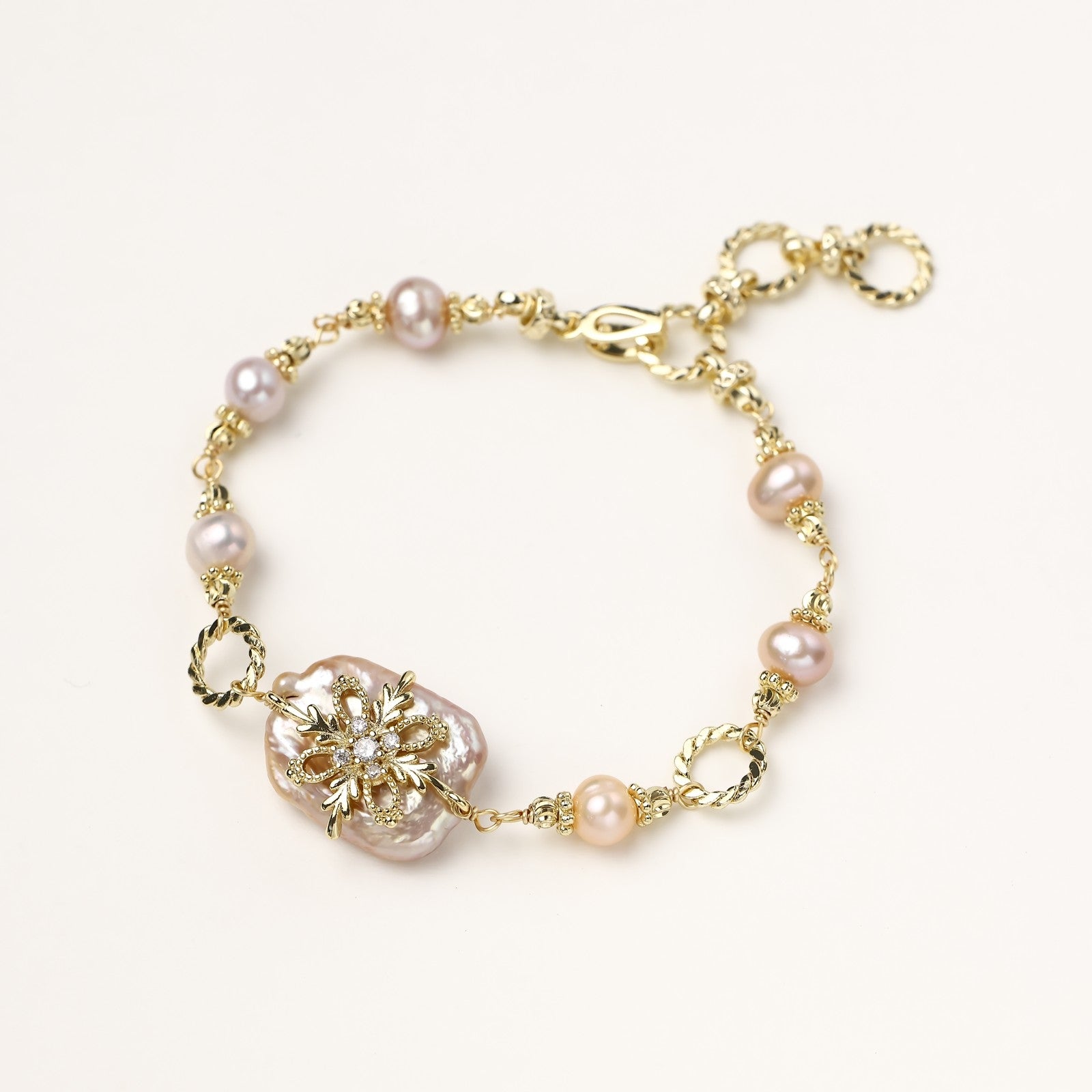 Gold-plated chain bracelet with baroque pearl centerpiece and floral charm, featuring mixed freshwater pearls.