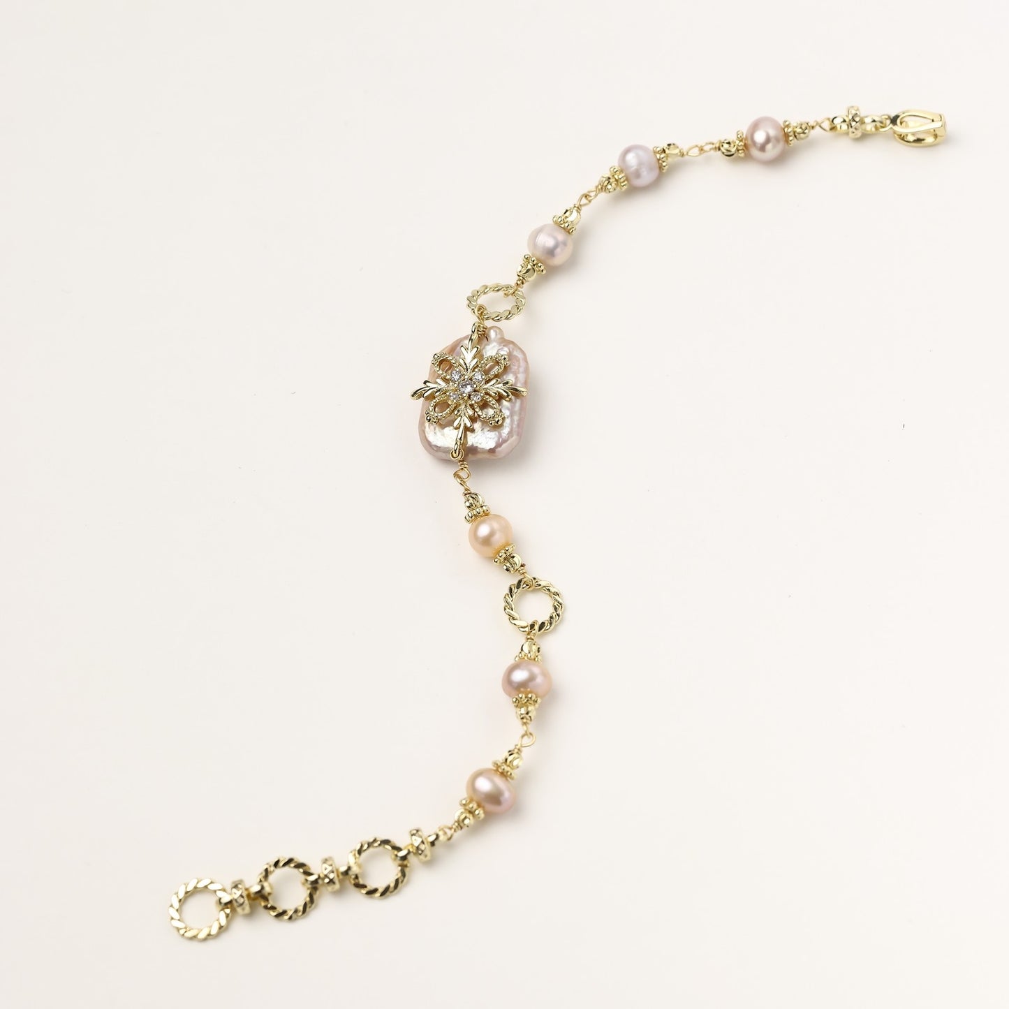 Gold-plated chain bracelet with baroque pearl centerpiece and floral charm, featuring mixed freshwater pearls.