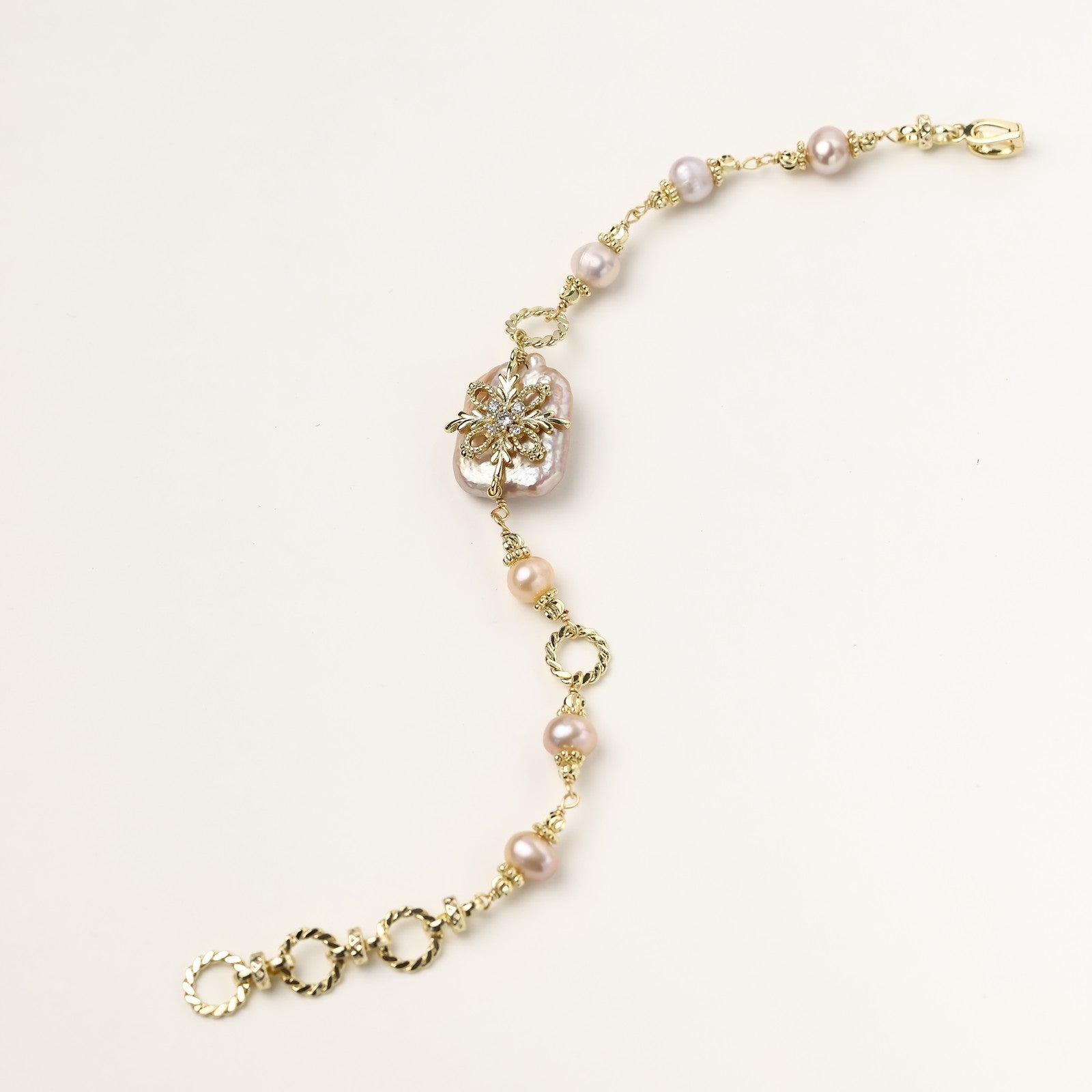 Gold-plated chain bracelet with baroque pearl centerpiece and floral charm, featuring mixed freshwater pearls.