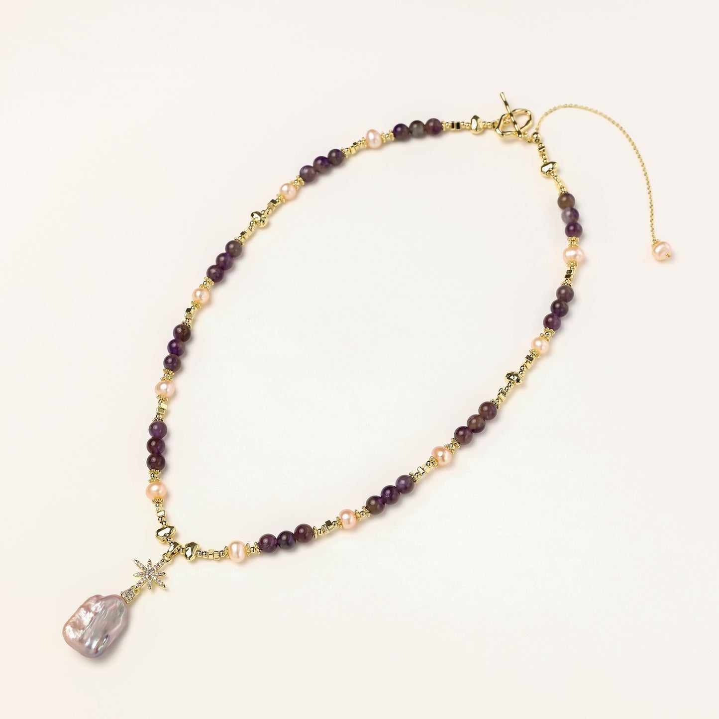Gold-plated necklace with purple amethyst beads, pink pearls, and iridescent baroque pearl pendant beneath crystal star charm