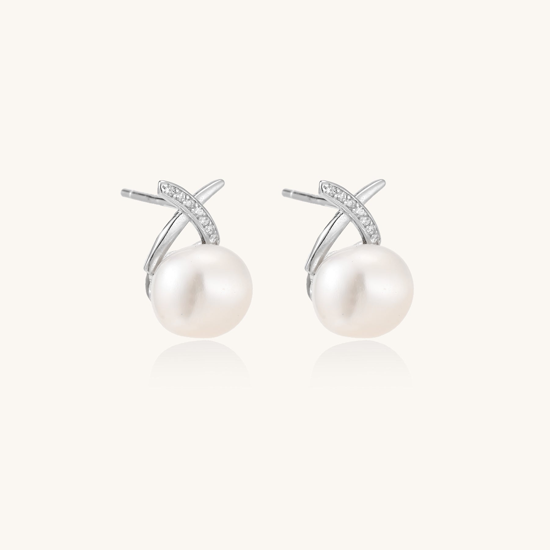 Sterling silver cross-shaped stud earrings with round freshwater pearls dangling below on white background.