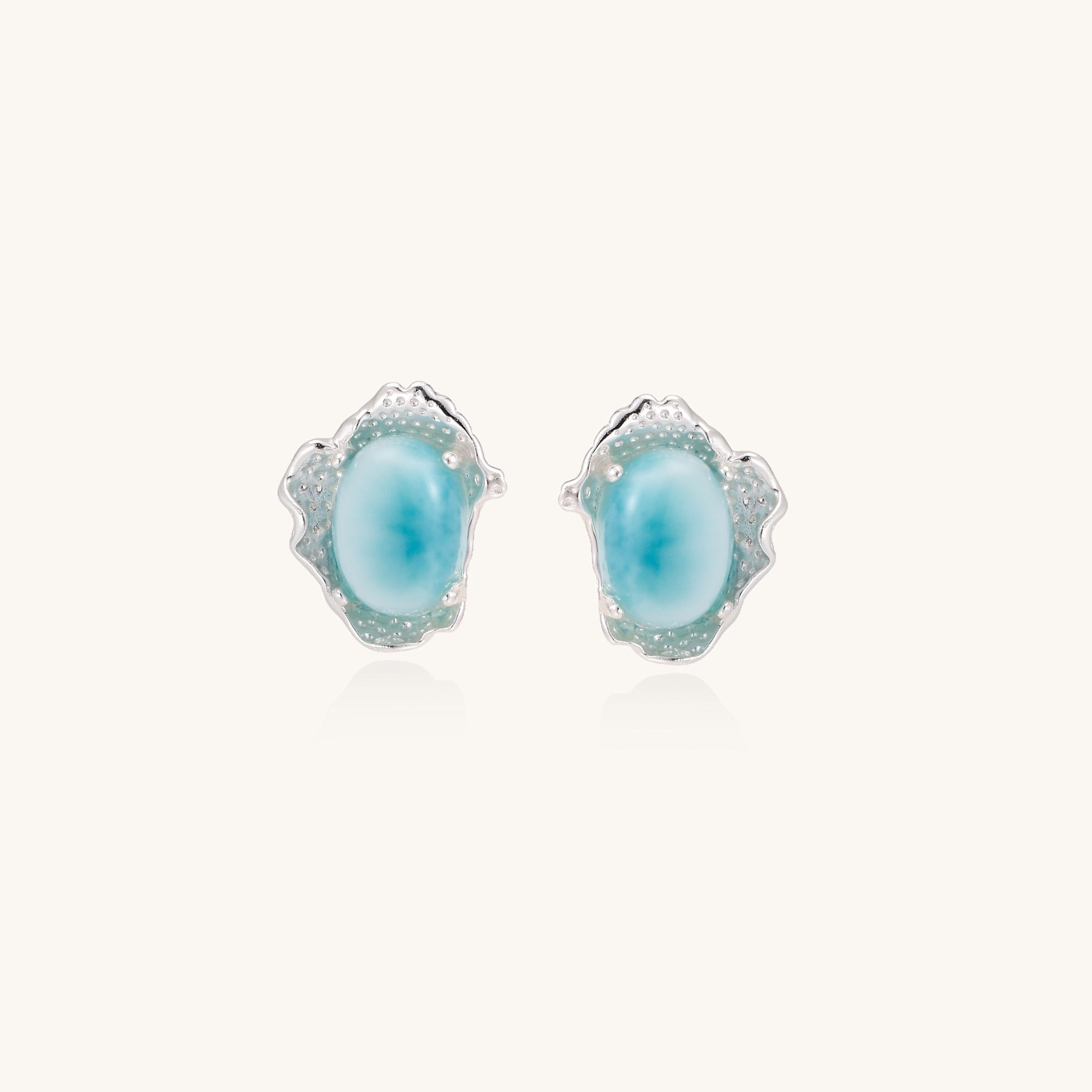 Close-up of sterling silver stud earrings with oval larimar stones in flowing wave-like settings on white background.