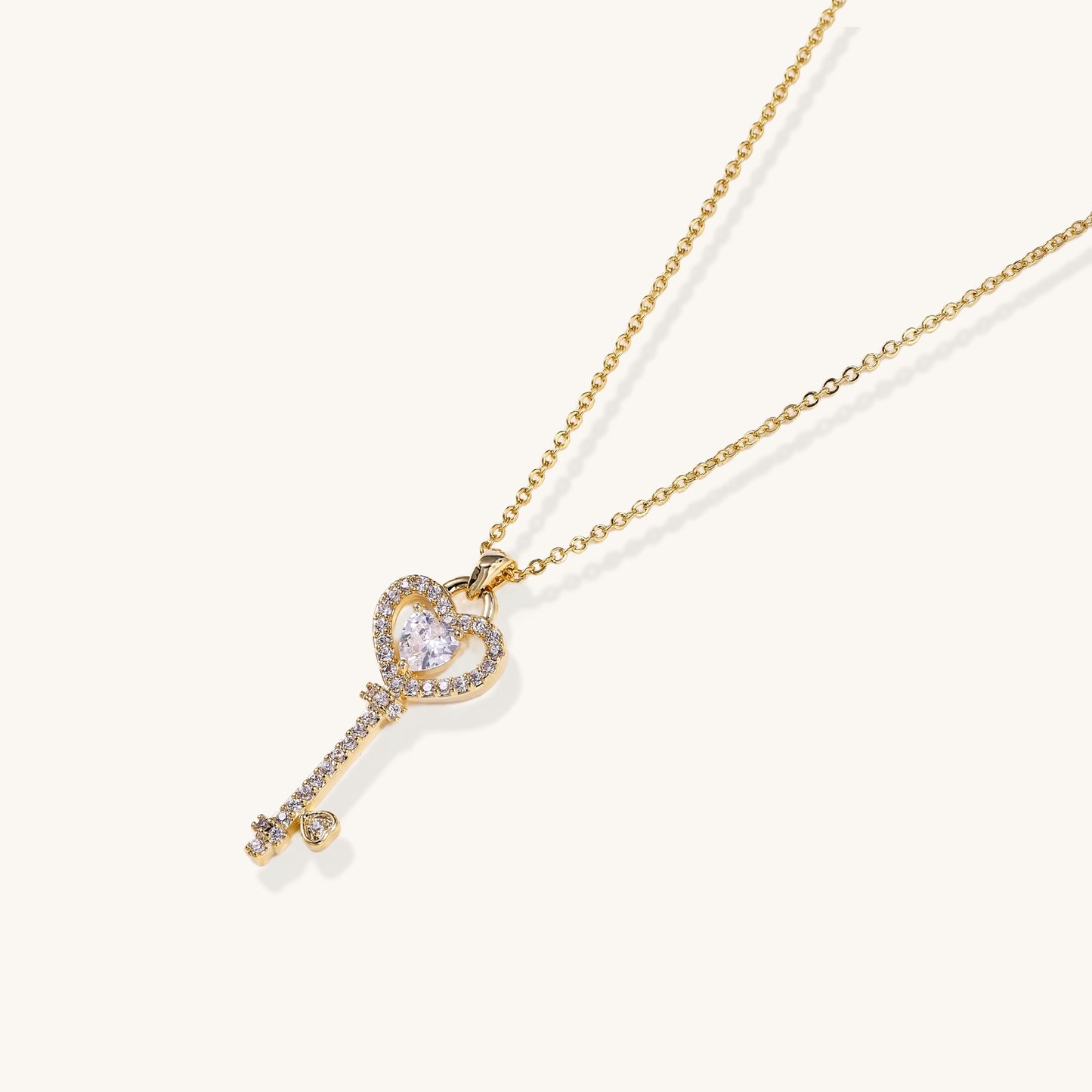 Gold-plated key pendant necklace with heart top and crystal embellishments on adjustable chain against cream background