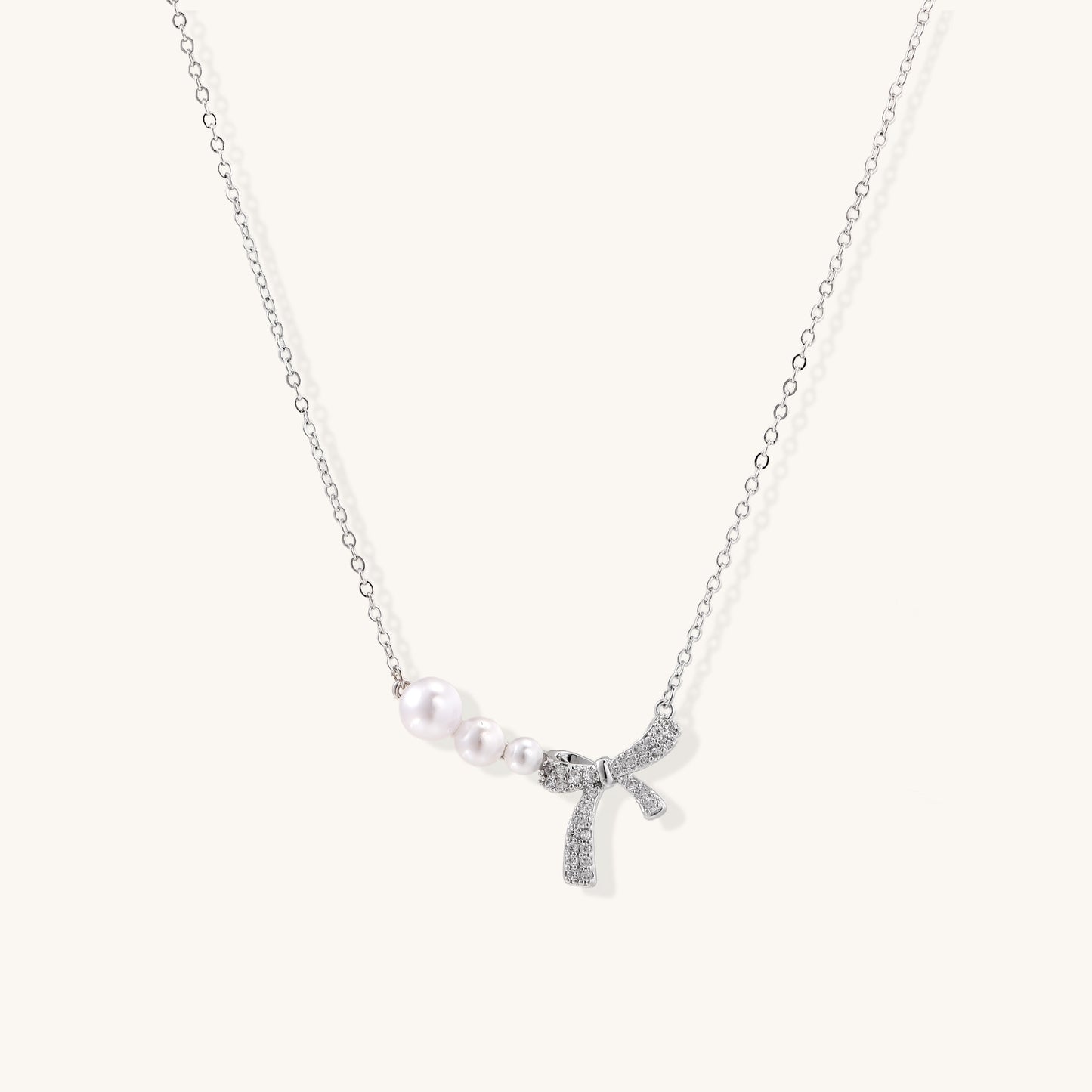 Dainty 14K gold plated necklace with freshwater pearls and sparkling bow charm on white background.