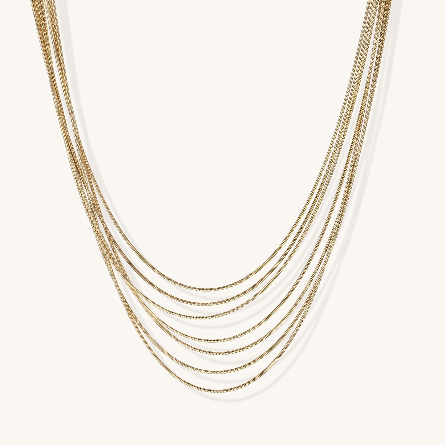 Multiple delicate gold-plated snake chains in graduated lengths on white background, adjustable layered necklace design.