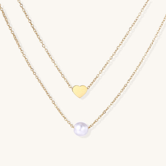 Two delicate gold-plated chains layered together, one with small heart pendant, another with cream pearl bead