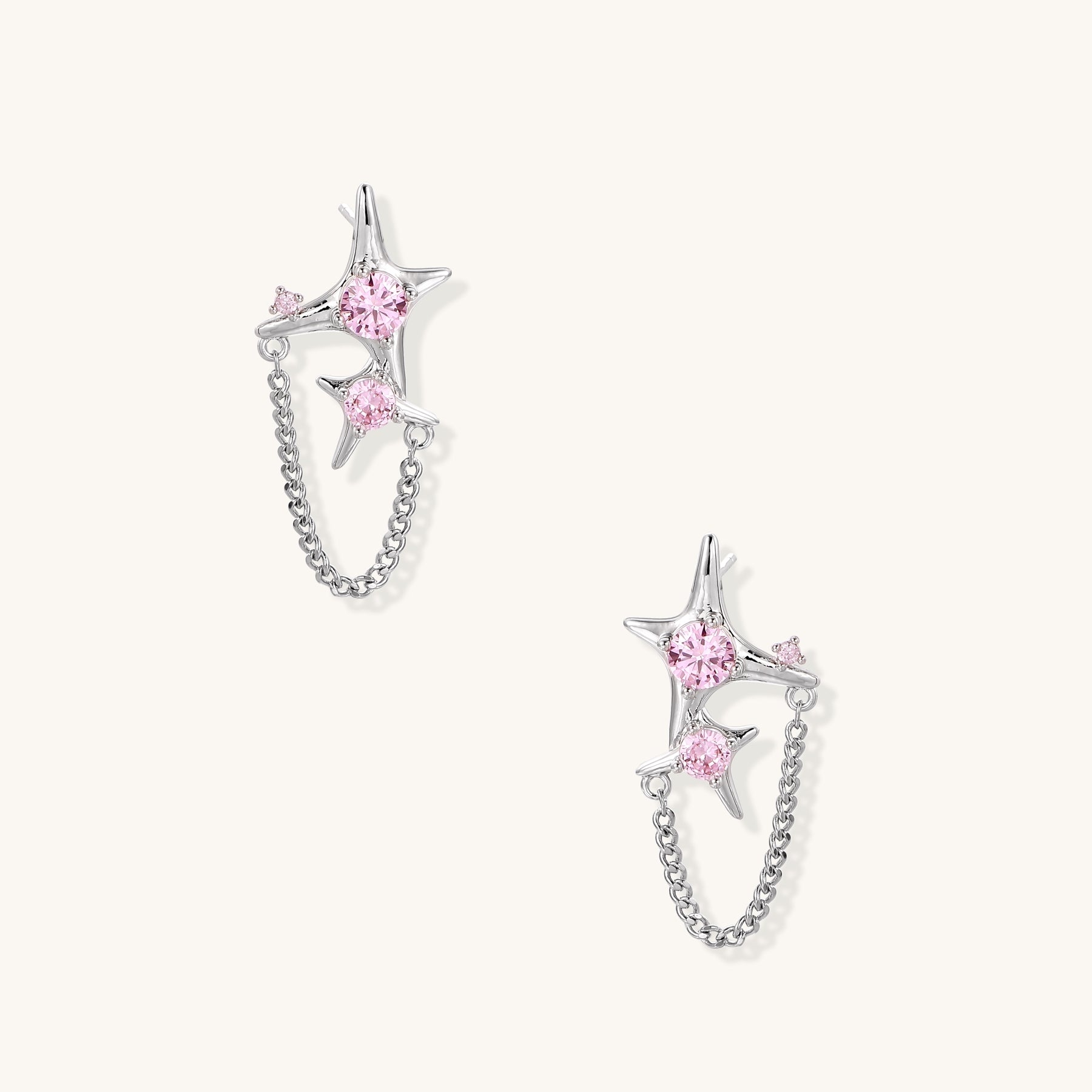 Gold-plated star earrings with pink zirconia stones connected by delicate chains on light background