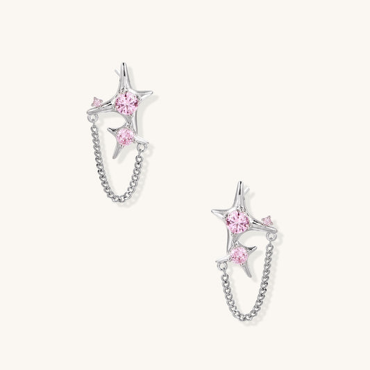 Gold-plated star earrings with pink zirconia stones connected by delicate chains on light background