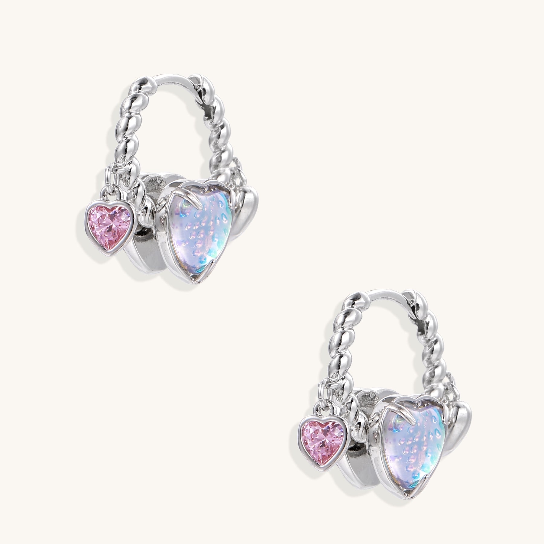 Gold-plated brass hoop earrings with three heart charms including iridescent turquoise and pink hearts on white background.
