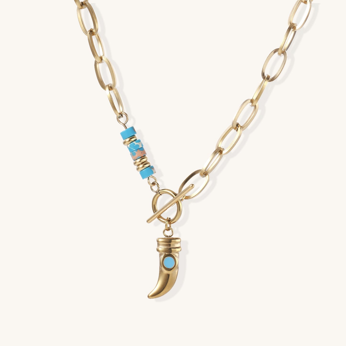 Gold-plated chain necklace with toggle clasp, turquoise beads, and curved horn pendant with inset turquoise stone on light background.