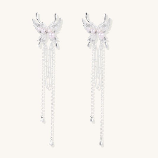 Elegant silver-plated drop earrings with wing-shaped tops, white pearl accents, and long chain tassels on white background.