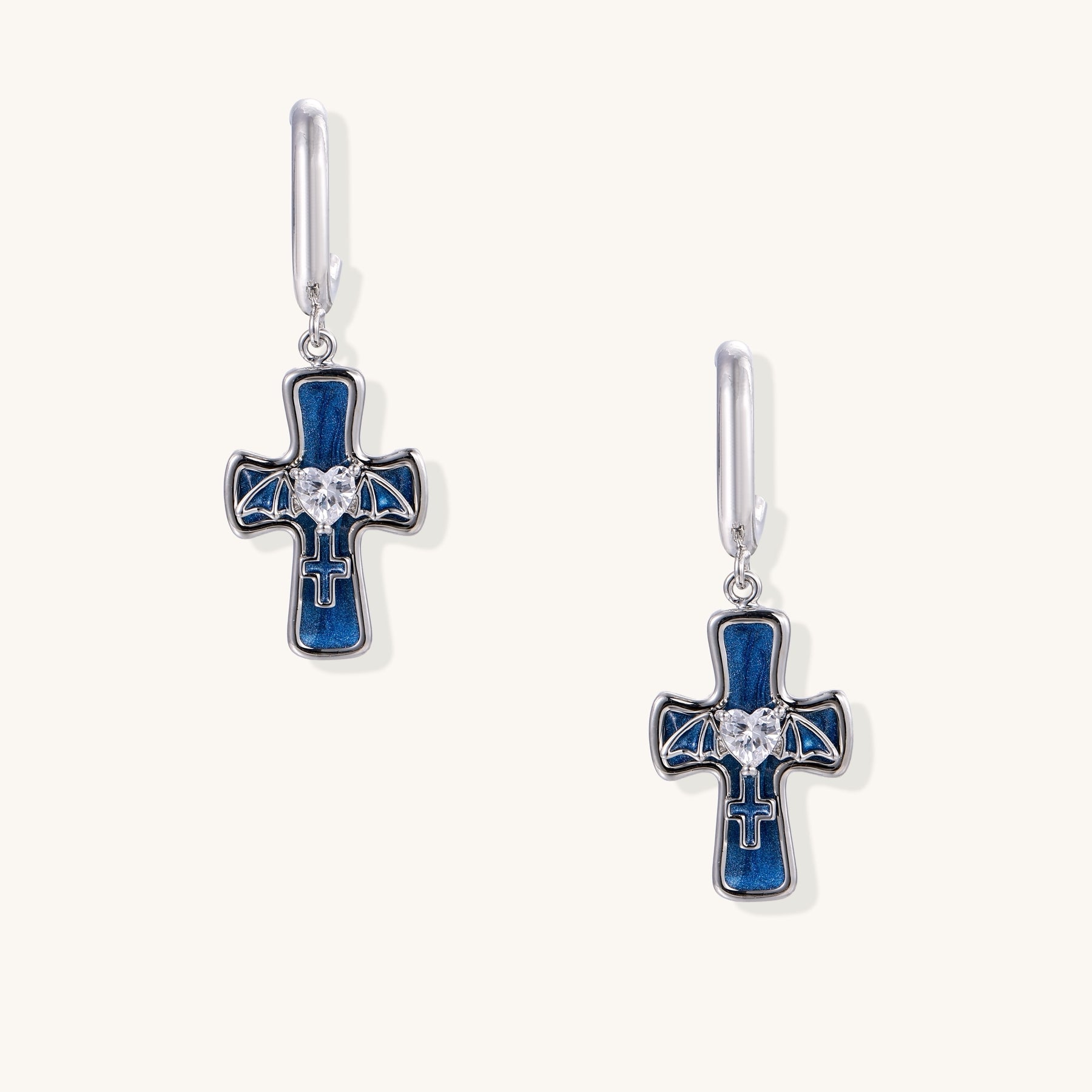 Gold-plated brass cross earrings with blue enamel, wing details, and heart-shaped zirconia stones on white background