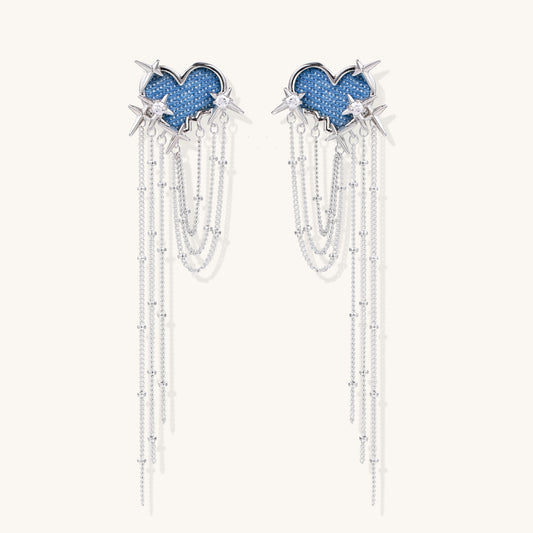 Long dangle earrings with blue denim heart shapes, silver star spikes, and multiple cascading chains on beige background.