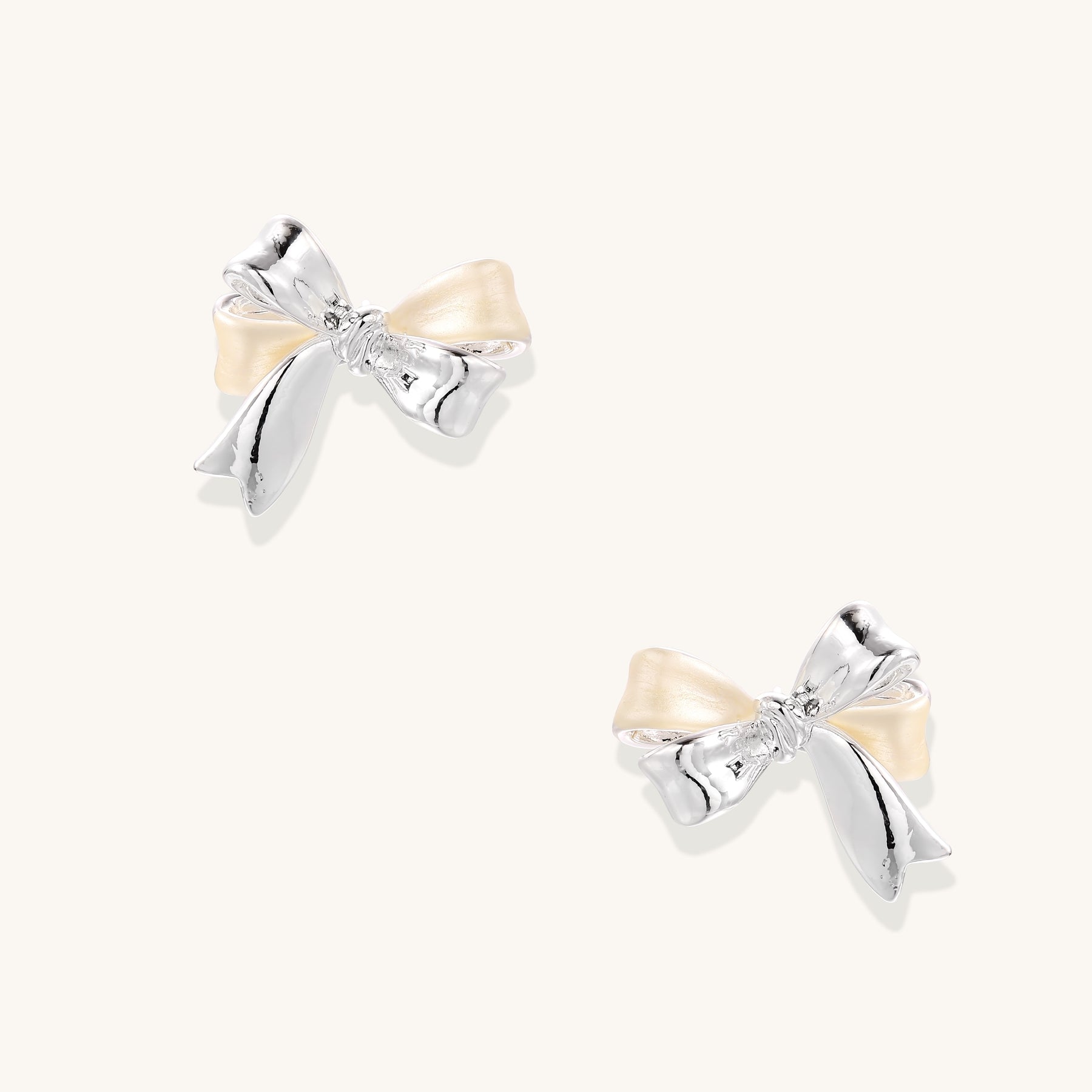 Close-up of bow-shaped stud earrings with 18K gold plated brass and silver details on white background.