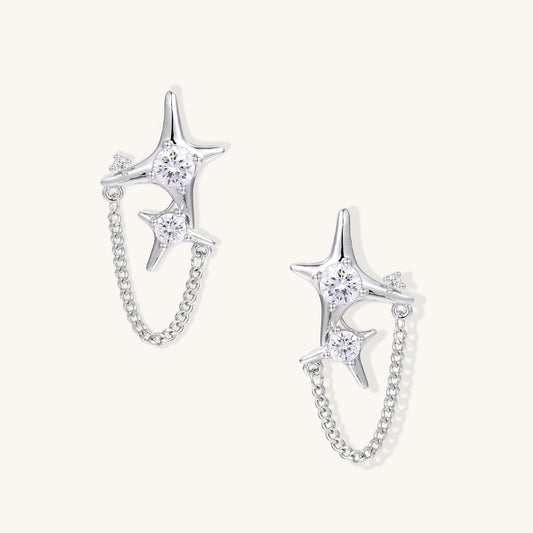 Delicate gold-plated star earrings with sparkling zirconia crystals connected by fine chains on cream background.