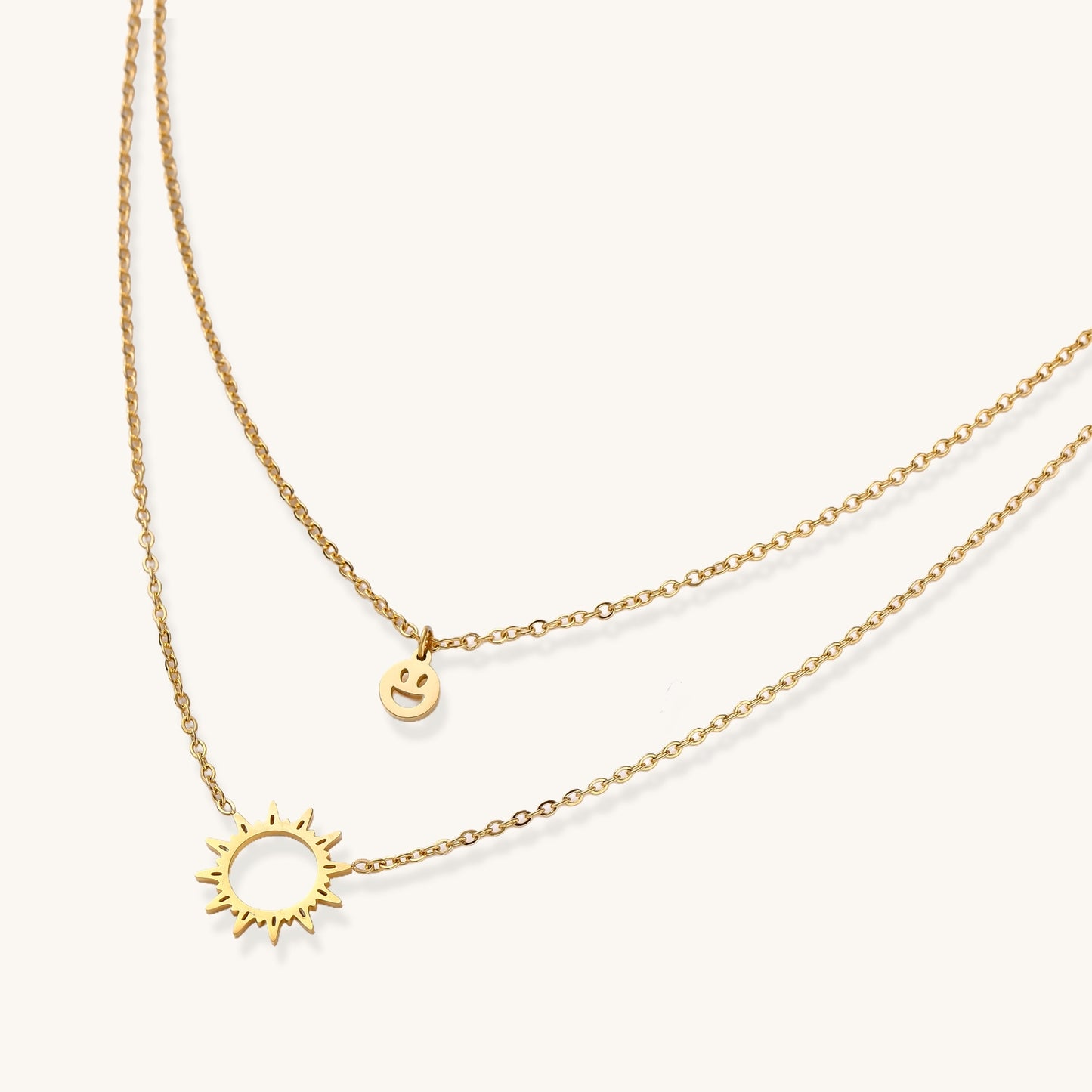 Delicate gold-plated layered necklace with smiley face and sun pendants on white background, showing adjustable chain.