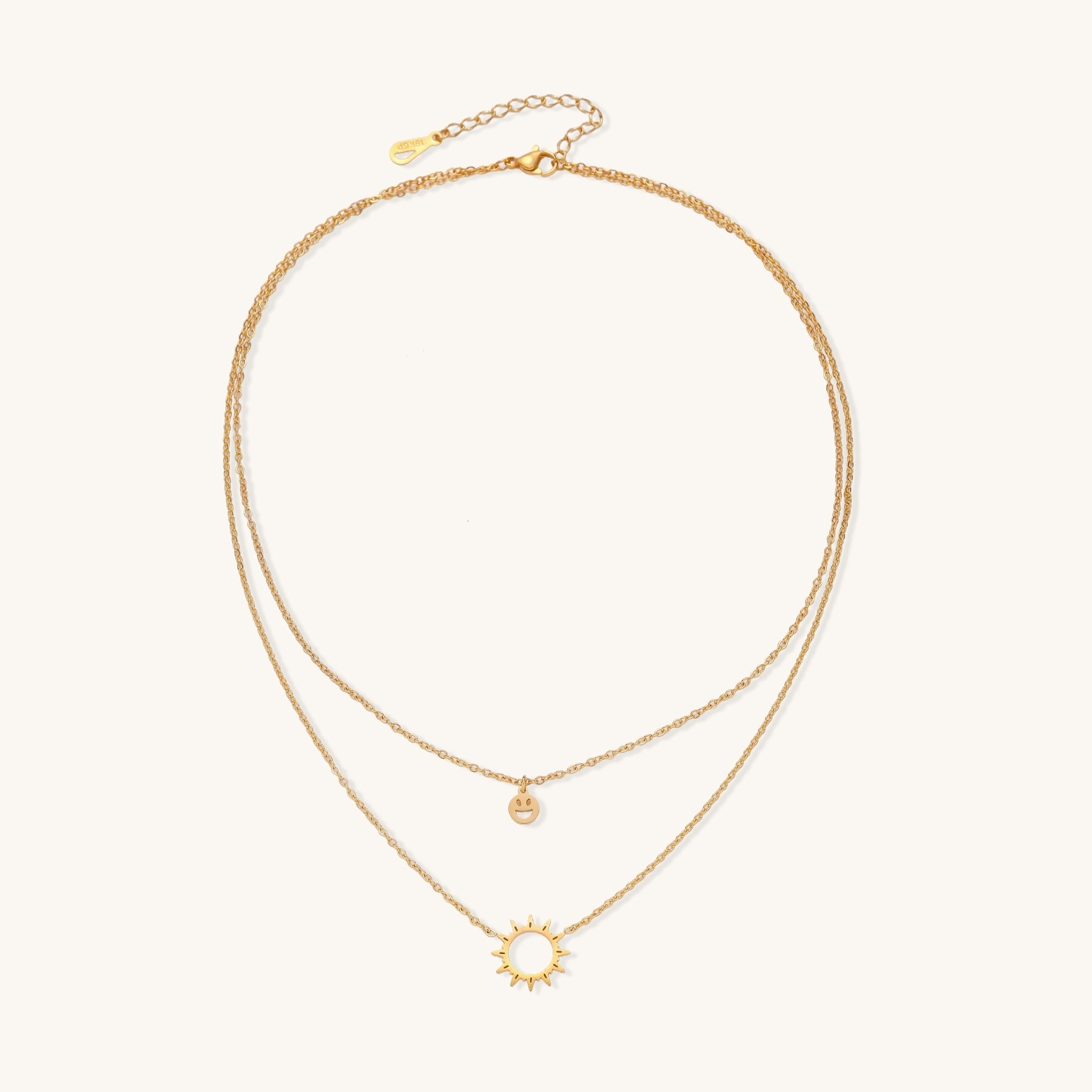 Delicate gold-plated layered necklace with smiley face and sun pendants on white background, showing adjustable chain.
